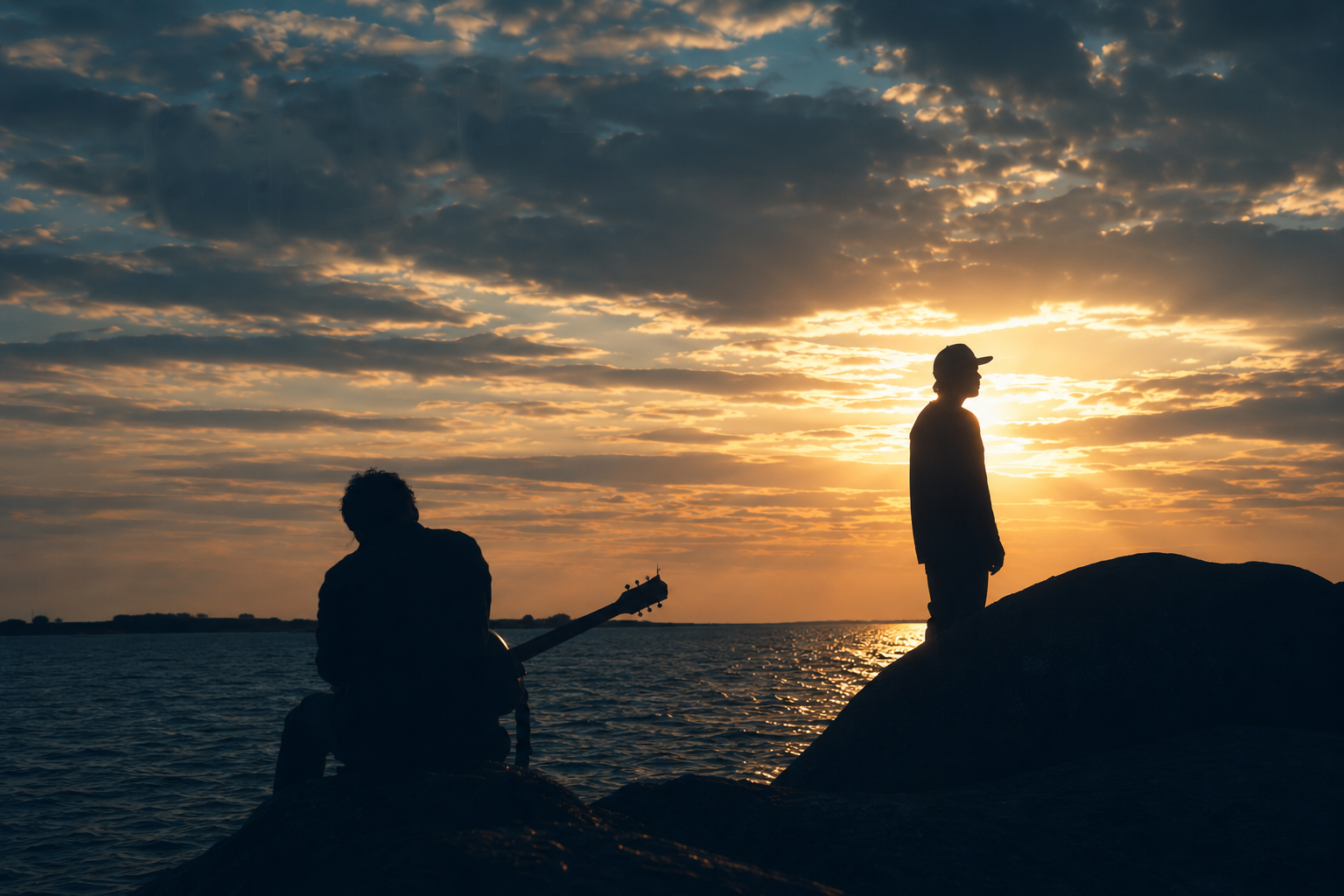 Kajaken – silhuetter mot solnedgången vid vattnet, en med gitarr och en stående på en klippa
